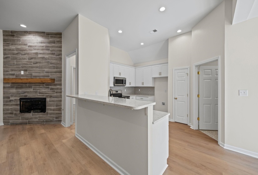 Kitchen featuring white cabinets, light stone counters, backsplash, stainless steel appliances, and light wood finished floors