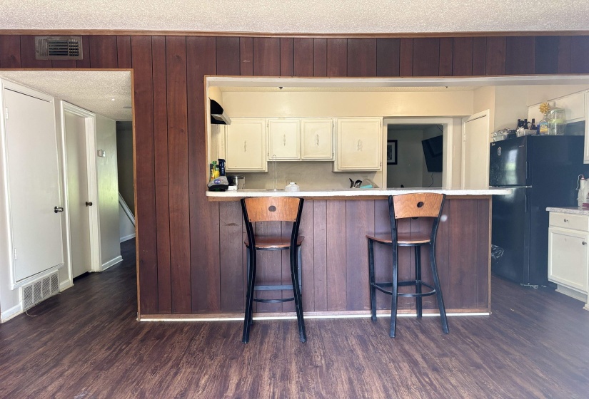 Kitchen featuring dark wood-style floors, freestanding refrigerator, light countertops, white cabinets, and a breakfast bar area