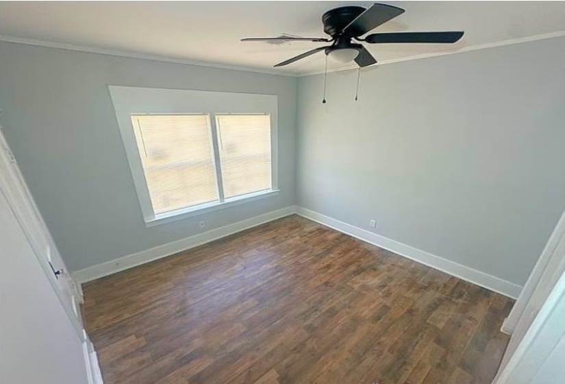 Empty room featuring dark wood-type flooring, crown molding, and a ceiling fan
