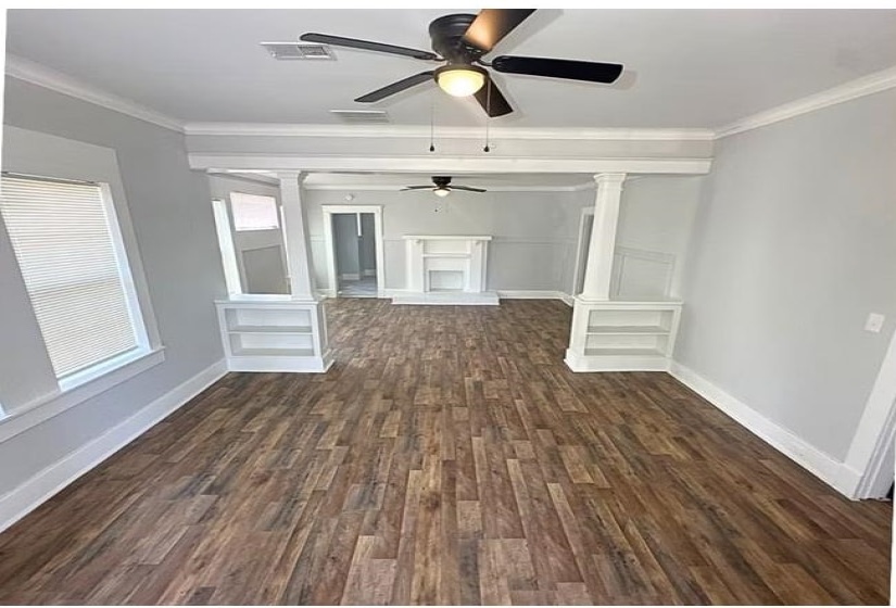 Unfurnished living room featuring dark wood-type flooring, a ceiling fan, and crown molding