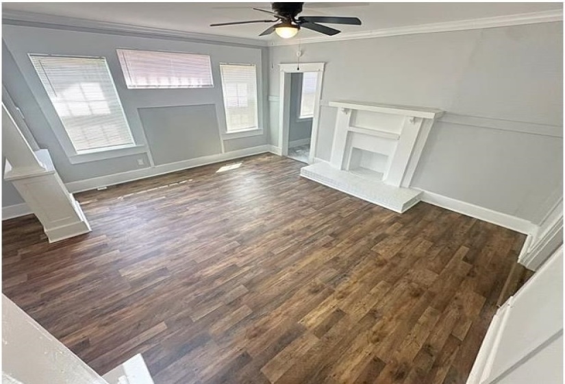 Unfurnished living room featuring ornamental molding, dark wood-style floors, ceiling fan, and a fireplace with raised hearth