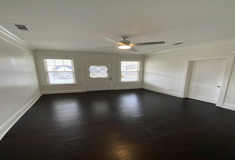 Empty room featuring dark wood-style floors, a ceiling fan, plenty of natural light, and crown molding
