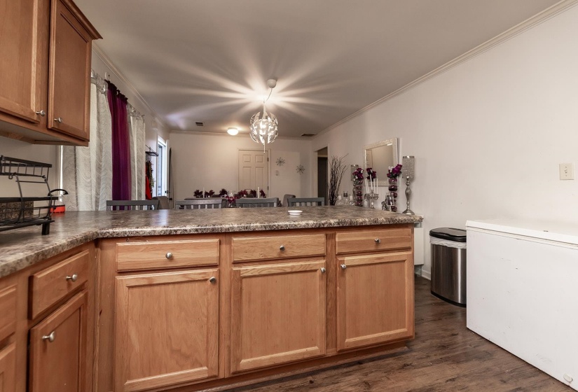 Kitchen with ornamental molding, dark wood-style flooring, a peninsula, dark countertops, and a chandelier