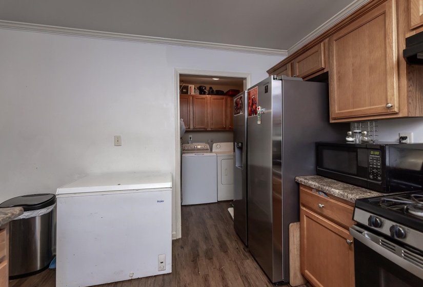 Kitchen featuring range with gas stovetop, dark wood-style flooring, washing machine and dryer, brown cabinets, and crown molding