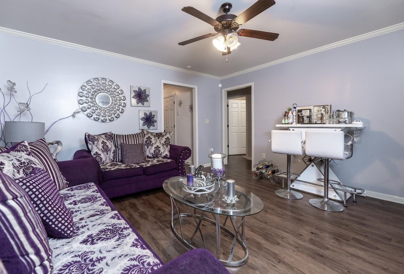 Living area with crown molding, dark wood-type flooring, and a ceiling fan