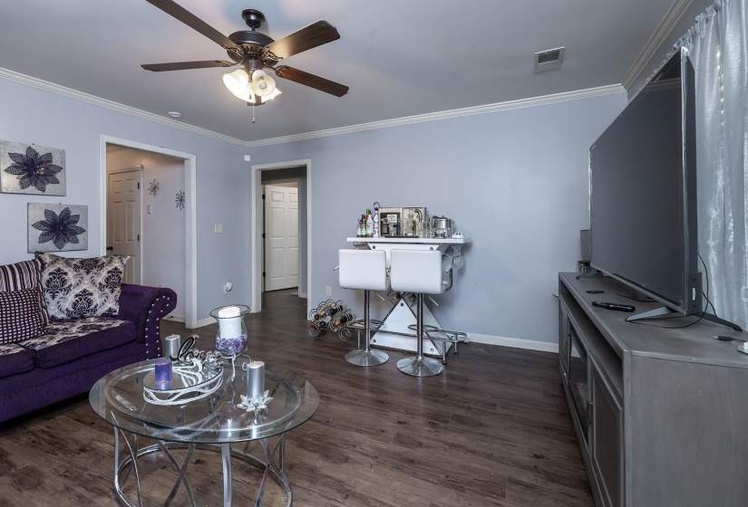 Living area with ornamental molding, dark wood-type flooring, and a ceiling fan