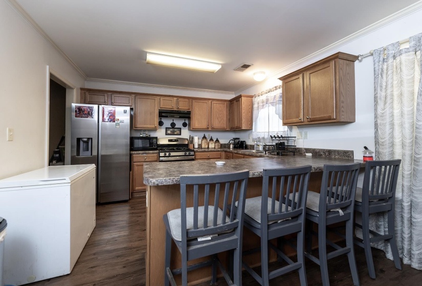Kitchen with appliances with stainless steel finishes, brown cabinetry, dark countertops, dark wood-style floors, and ornamental molding