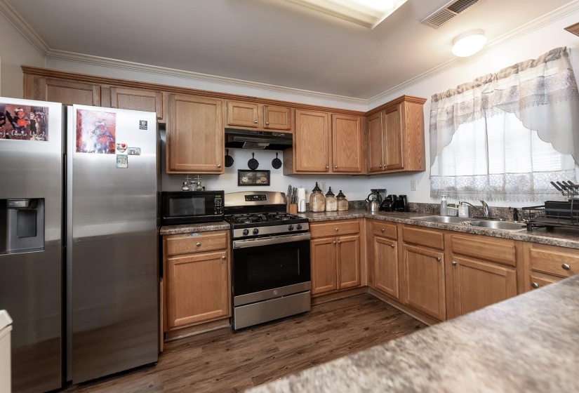 Kitchen featuring appliances with stainless steel finishes, ornamental molding, dark wood-style flooring, brown cabinets, and under cabinet range hood