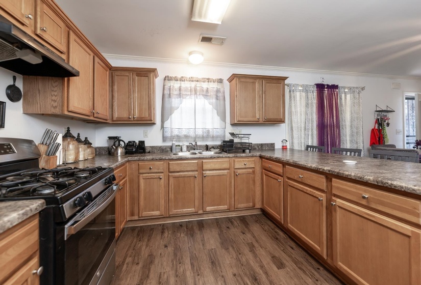 Kitchen featuring stainless steel gas range oven, healthy amount of natural light, under cabinet range hood, dark wood-style flooring, and ornamental molding