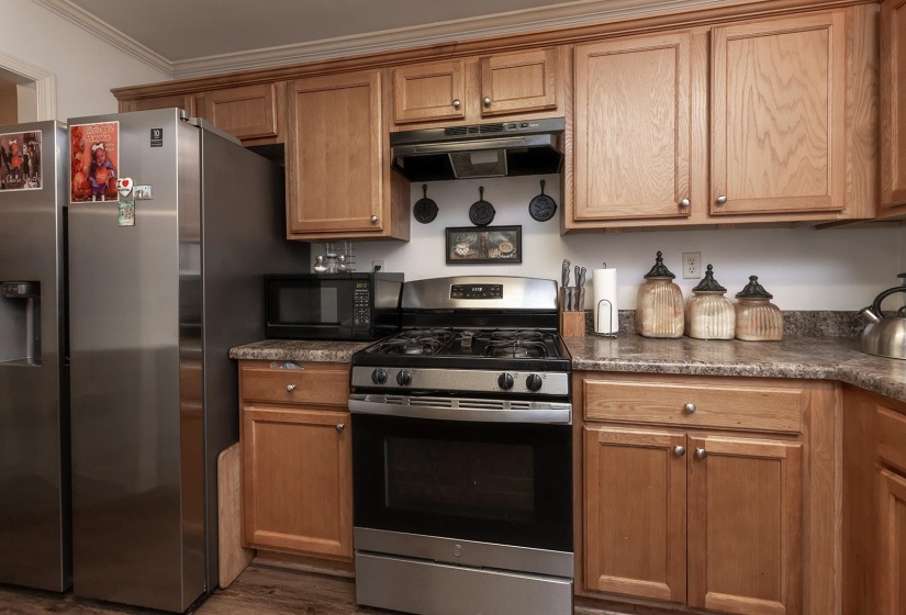 Kitchen with stainless steel appliances, ventilation hood, dark countertops, brown cabinetry, and crown molding