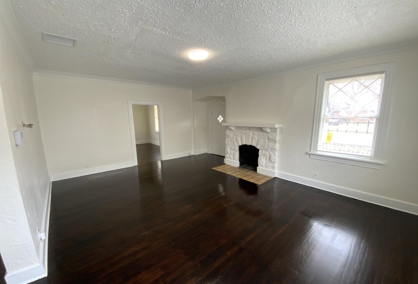 Unfurnished living room featuring dark wood-style flooring, a stone fireplace, a textured ceiling, and crown molding