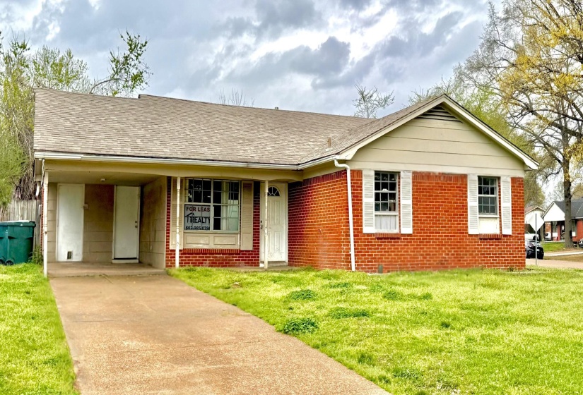 Ranch-style house featuring a carport, brick siding, concrete driveway, a front yard, and a shingled roof