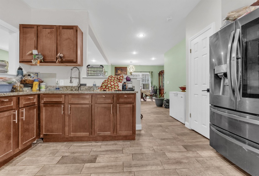 Kitchen with stainless steel fridge, wood finish cabinetry, a peninsula, light stone counters, and recessed lighting