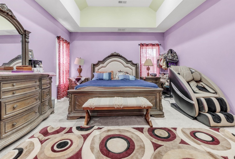 Bedroom featuring a raised ceiling, light colored carpet, and lofted ceiling