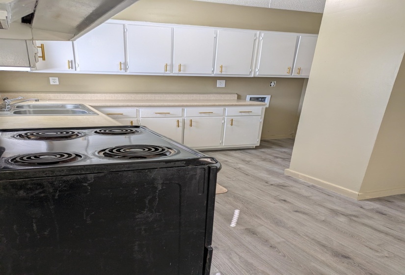 Kitchen with electric range, white cabinets, light countertops, light wood-style flooring, and range hood