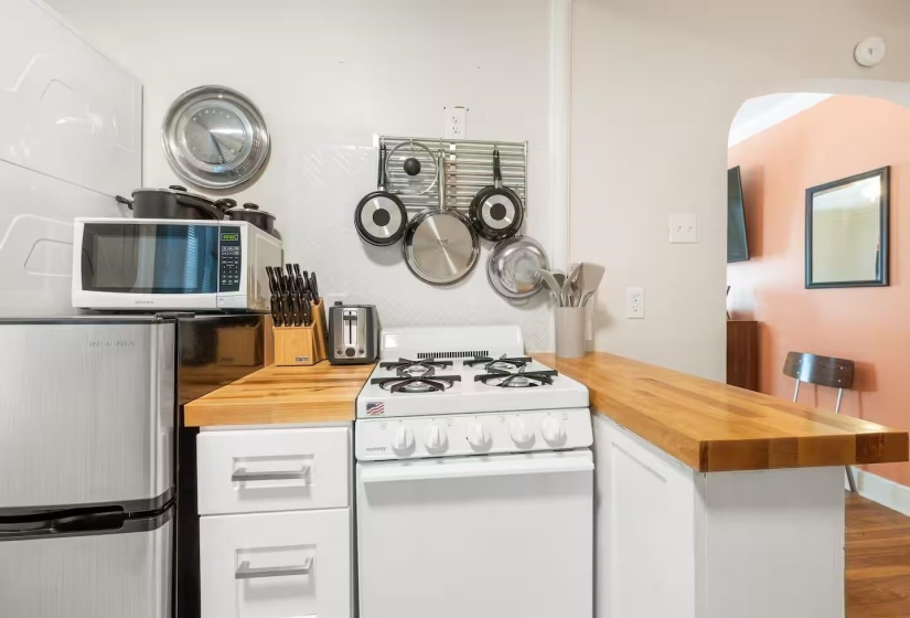 Kitchen with wood counters, white appliances, white cabinetry, a peninsula, and wood finished floors