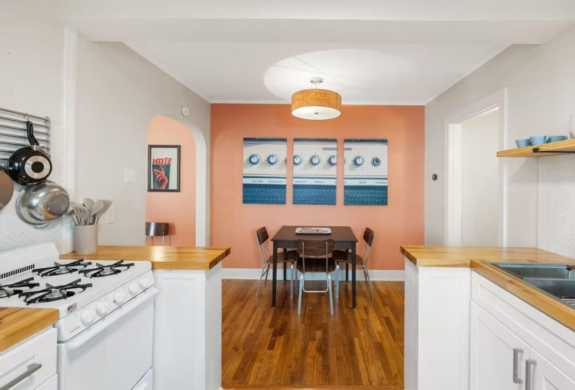 Kitchen with butcher block counters, gas range gas stove, white cabinetry, dark wood-type flooring, and crown molding