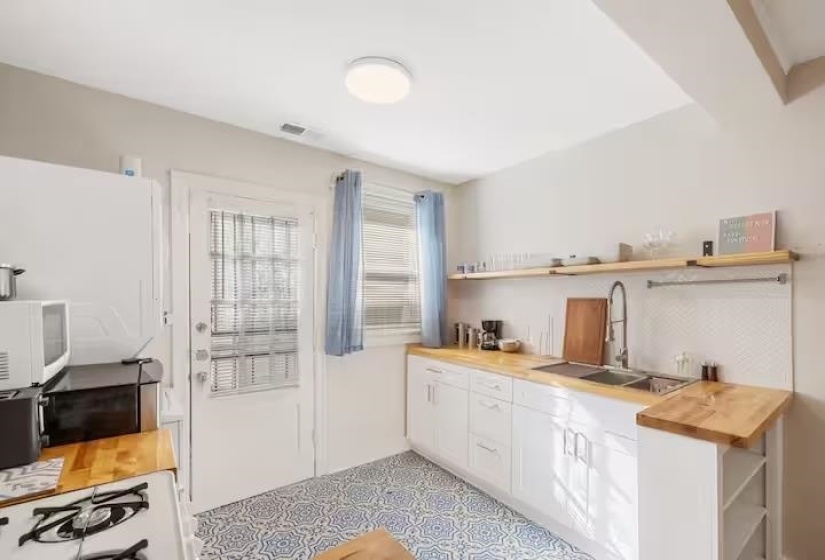 Kitchen with white cabinetry, open shelves, butcher block counters, and white appliances