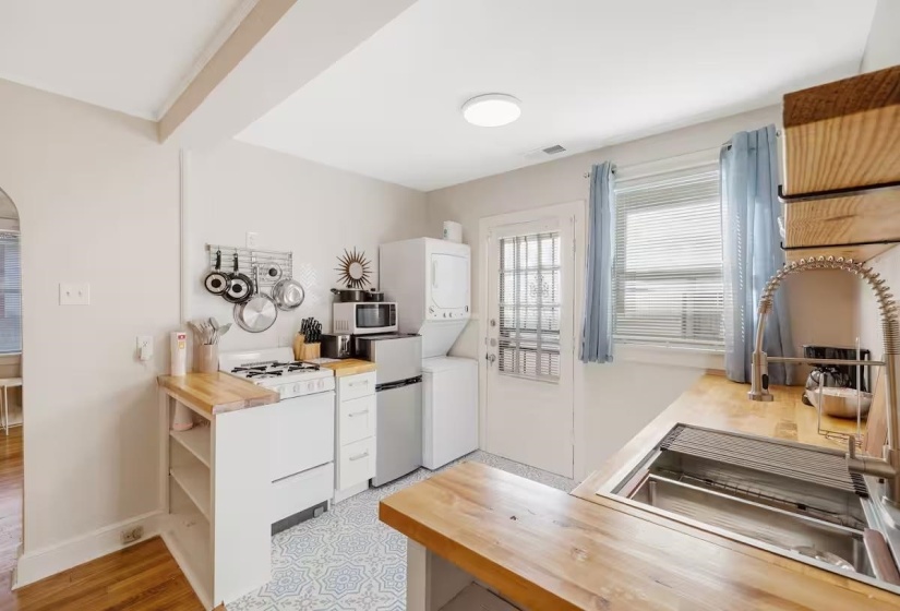 Kitchen featuring wooden counters, white cabinetry, stainless steel appliances, stacked washer / dryer, and arched walkways