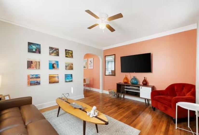 Living area featuring ornamental molding, wood finished floors, arched walkways, and a ceiling fan