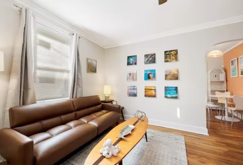 Living room with arched walkways, wood finished floors, crown molding, and a ceiling fan