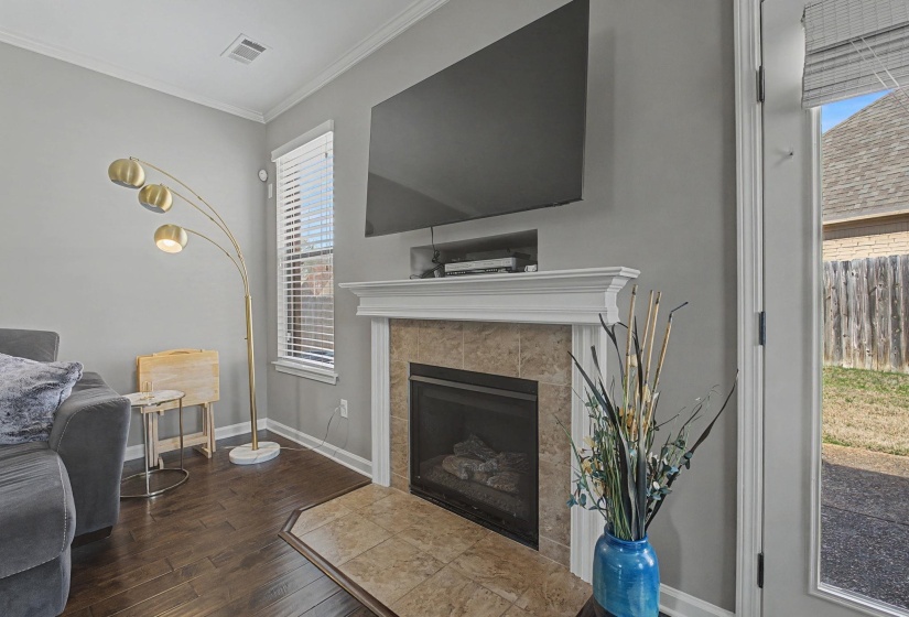 Living room with crown molding, dark wood-type flooring, and a tiled fireplace