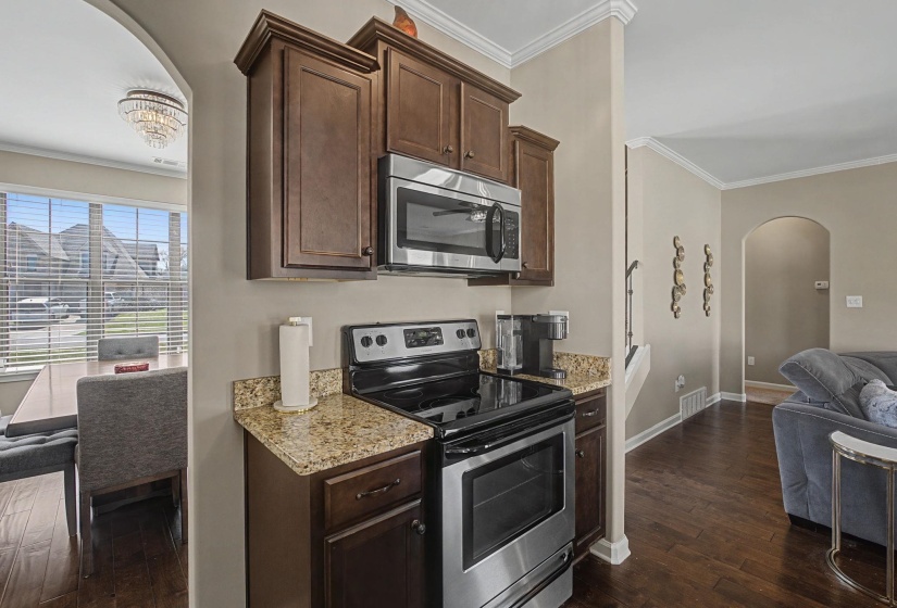 Kitchen with arched walkways, stainless steel appliances, dark wood finish cabinetry, crown molding, and light stone counters
