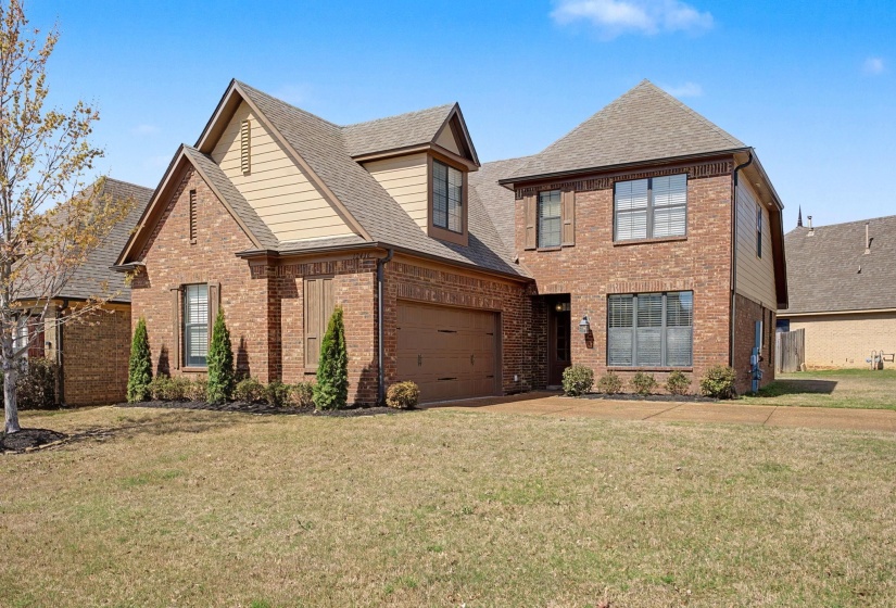 View of front facade with roof with shingles, a front lawn, and brick siding