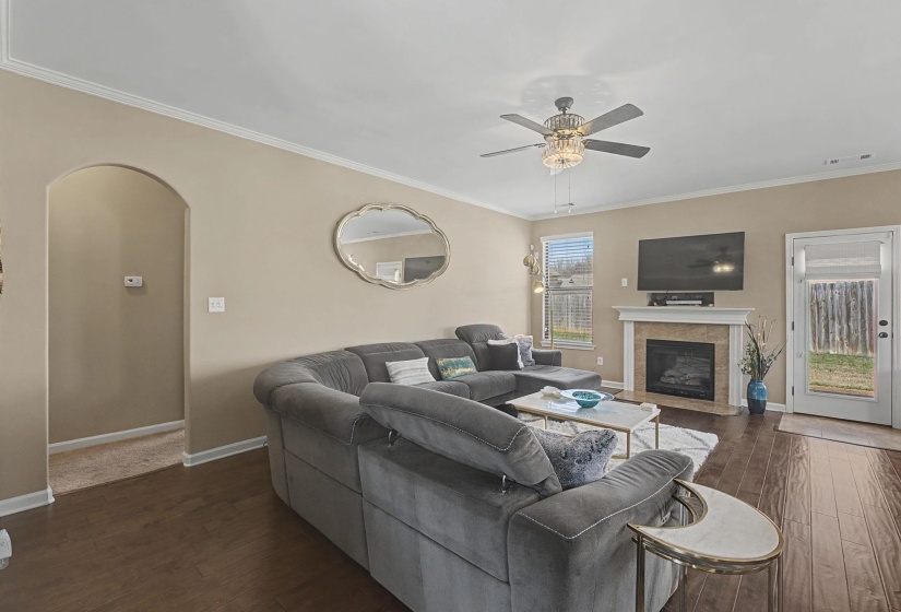 Living room featuring arched walkways, dark wood-style floors, ceiling fan, a fireplace, and ornamental molding