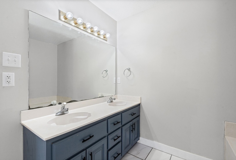 Bathroom featuring double vanity, light marble finish flooring, and a bathtub