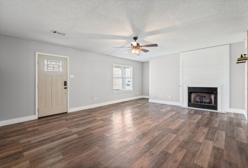 Spacious living room featuring a textured ceiling, ceiling fan, dark wood-style flooring, and a large fireplace