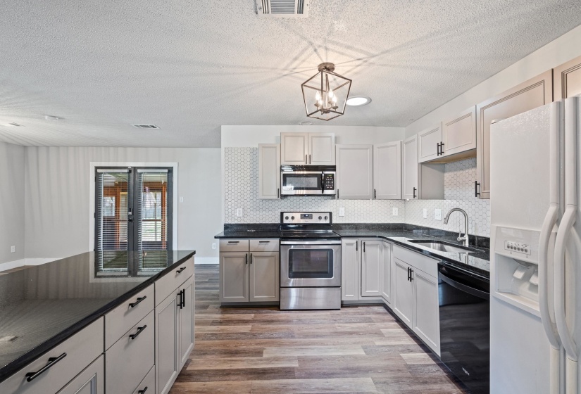 Kitchen with stainless steel appliances, light wood-style flooring, decorative backsplash, a textured ceiling, and a chandelier