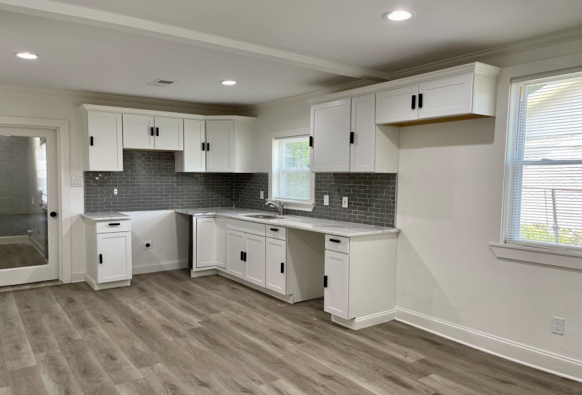Kitchen with white cabinetry, crown molding, light stone counters, light wood-type flooring, and decorative backsplash