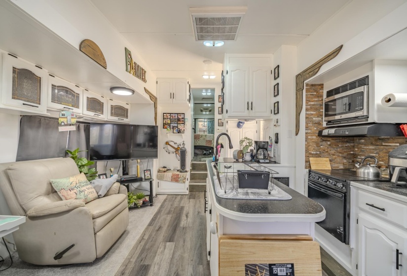 Kitchen with white cabinetry, light wood-style flooring, black electric range oven, dark countertops, and stainless steel microwave