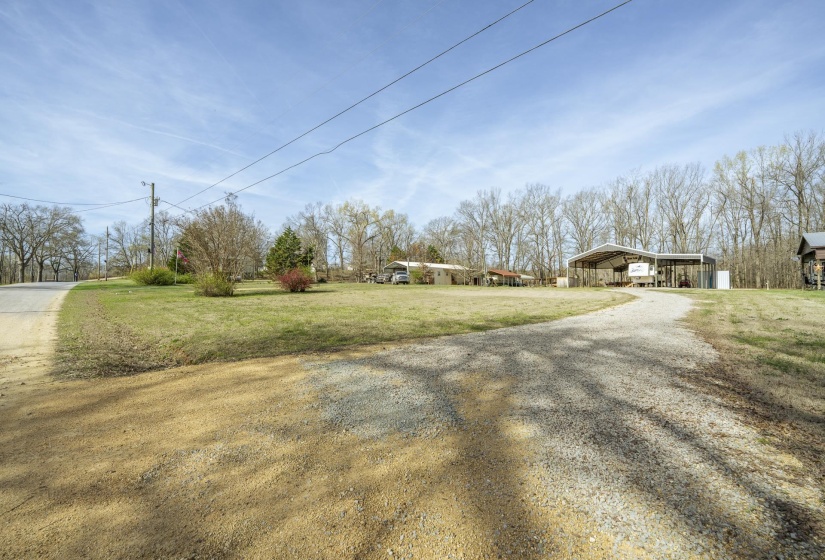 View of green lawn with a detached carport and gravel driveway