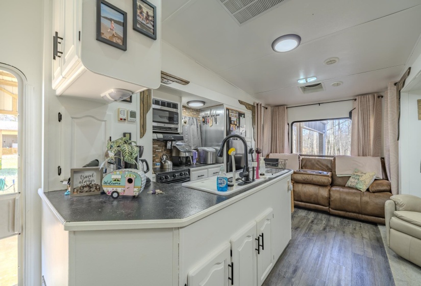 Kitchen with open floor plan, white cabinets, dark wood-style flooring, dark countertops, and stainless steel microwave