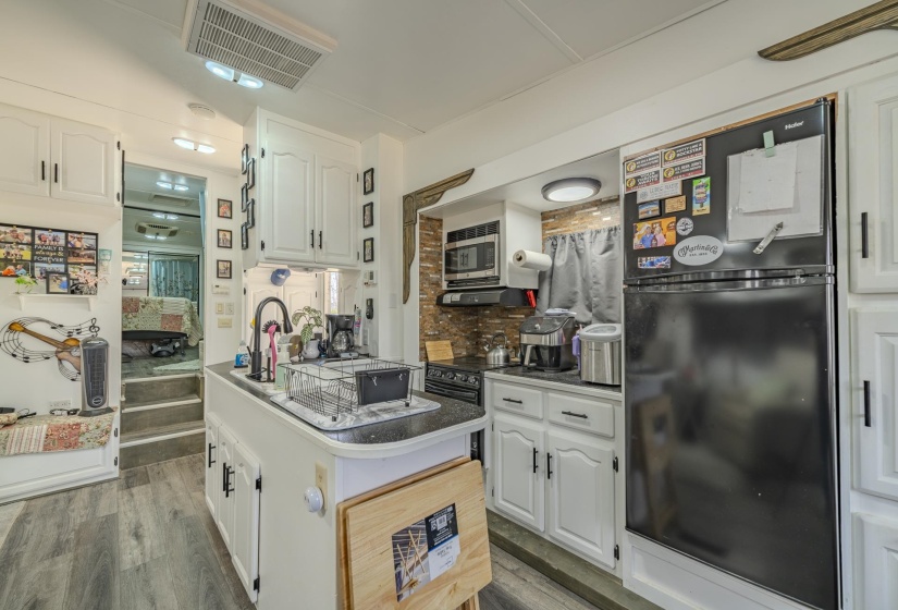 Kitchen featuring white cabinetry, black appliances, dark wood-type flooring, decorative backsplash, and dark countertops