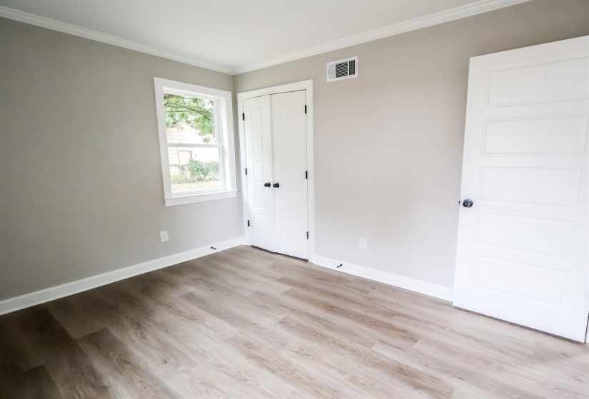 Unfurnished bedroom with crown molding, light wood-style flooring, and a closet