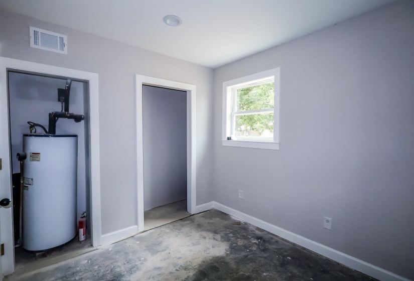 Unfurnished bedroom with unfinished concrete floors and water heater