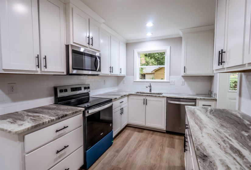 Kitchen featuring stainless steel appliances, white cabinetry, light wood-type flooring, light stone counters, and crown molding