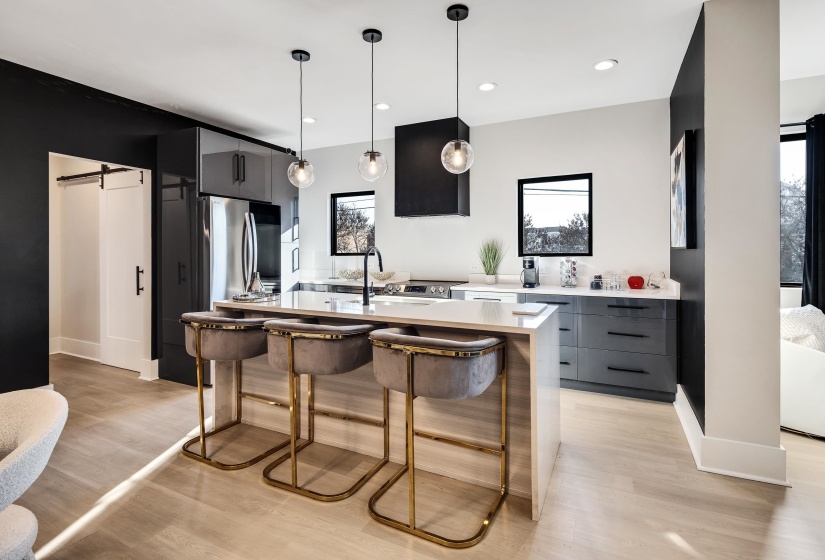 Kitchen with a barn door, modern cabinets, a kitchen breakfast bar, a kitchen island with sink, and hanging light fixtures
