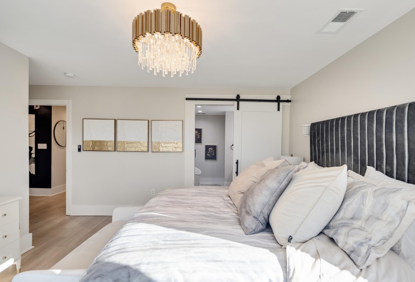 Bedroom with a barn door, ensuite bath, a chandelier, and wood finished floors