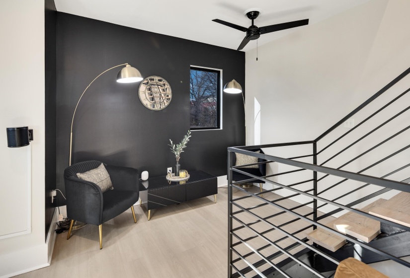 Living area with ceiling fan, light wood-style floors, an accent wall, and an upstairs landing