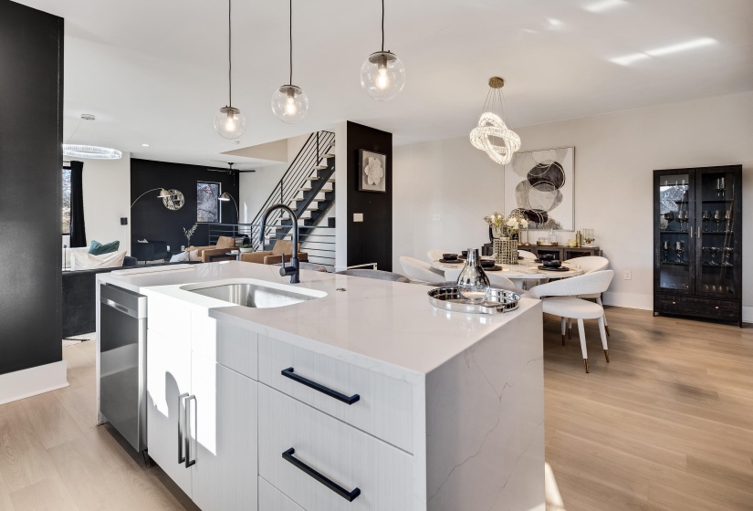 Kitchen featuring modern cabinets, white cabinetry, light stone countertops, decorative light fixtures, and a kitchen island with sink