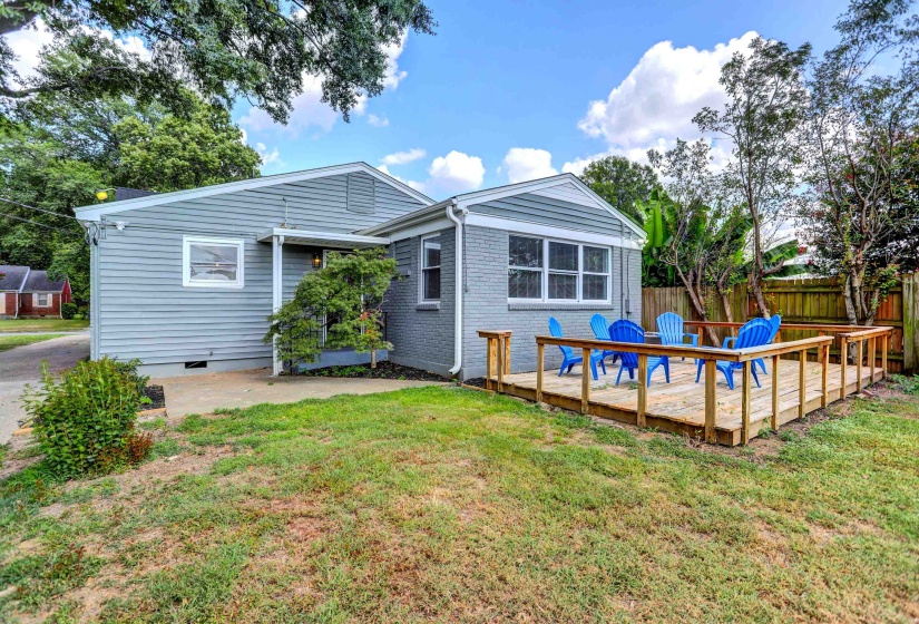 Back of property with brick siding, a deck, fence, and a lawn
