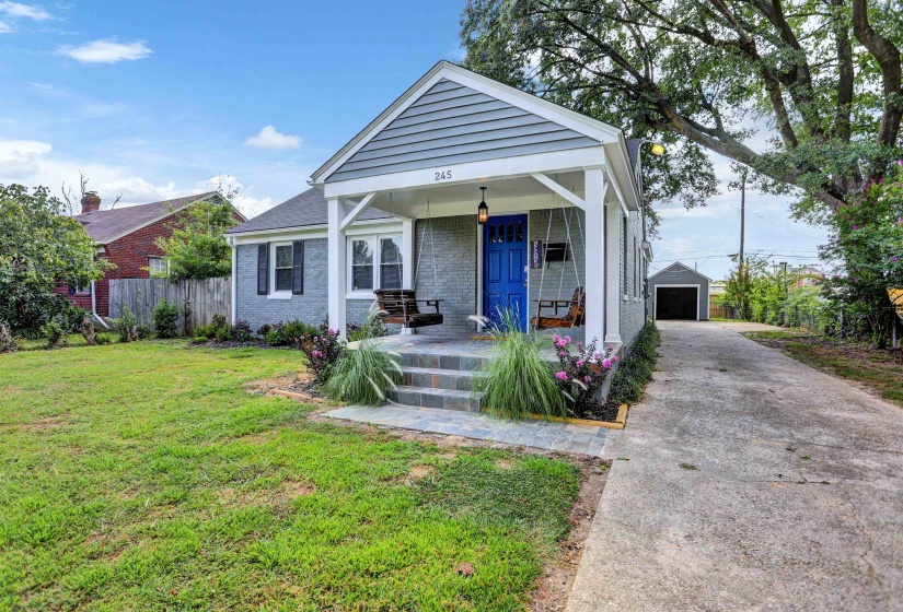View of front of house featuring an outdoor structure, a front yard, brick siding, a porch, and fence