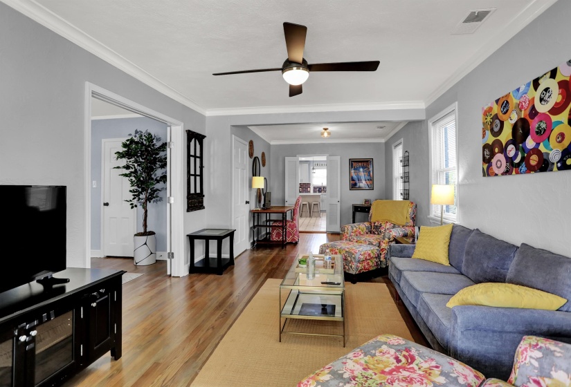 Living room featuring crown molding, visible vents, a ceiling fan, and wood finished floors