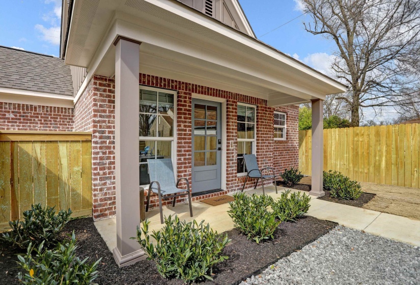 Doorway to property with a porch, brick siding, fence, and a shingled roof
