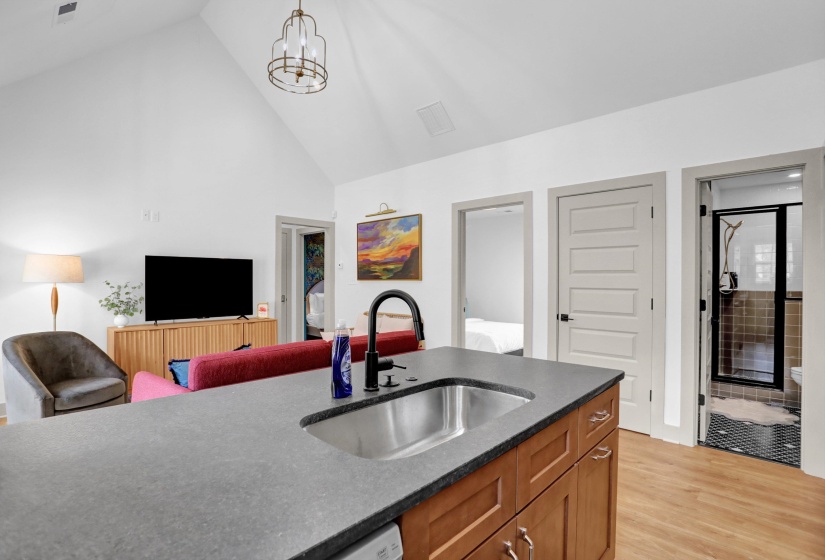 Kitchen featuring a sink, light wood-type flooring, dark countertops, brown cabinetry, and high vaulted ceiling