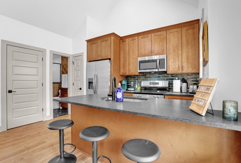 Kitchen featuring brown cabinetry, dark countertops, vaulted ceiling, and appliances with stainless steel finishes